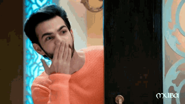 a man in an orange sweater is covering his mouth with his hands