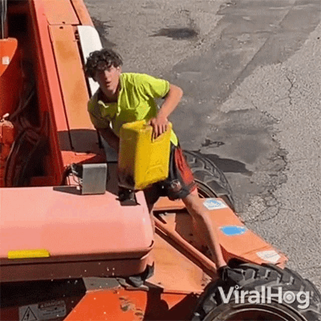 a man is standing on the back of a tractor holding a yellow can .