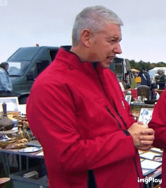 a man in a red jacket is standing in front of a table full of objects .