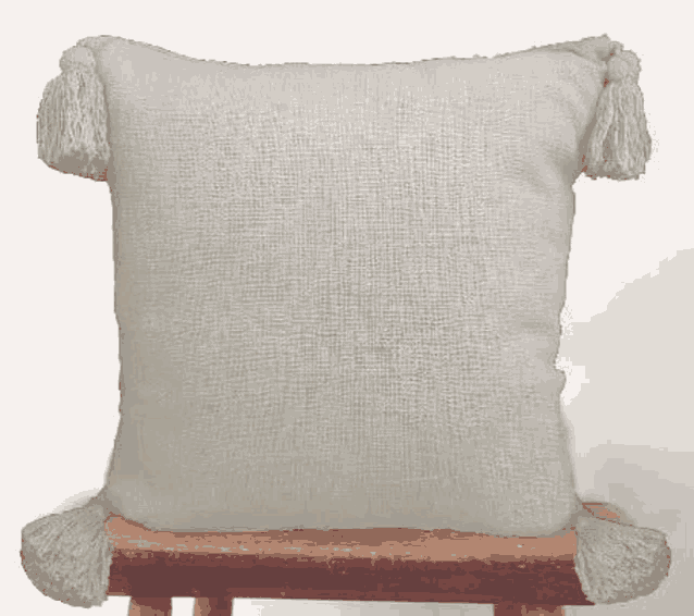 a white pillow with tassels on it is sitting on a wooden stool .