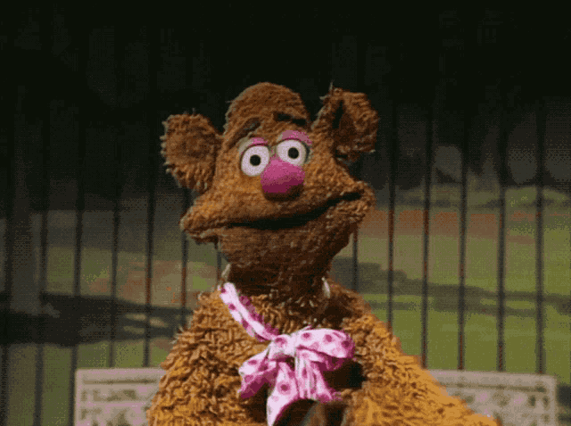 a brown teddy bear with a pink nose and a pink bow around his neck