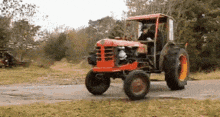 a red tractor is driving down a dirt road in a field