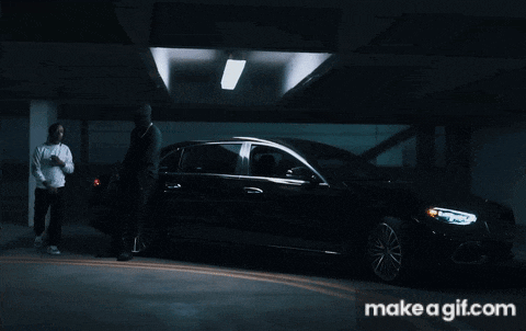 two men standing next to a car in a dark garage with makeagif.com in the corner