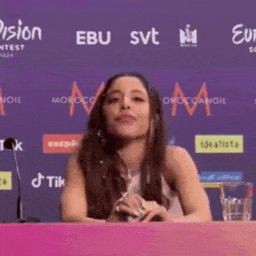 a woman is sitting at a table with a glass of water in front of a wall that says tik tok .
