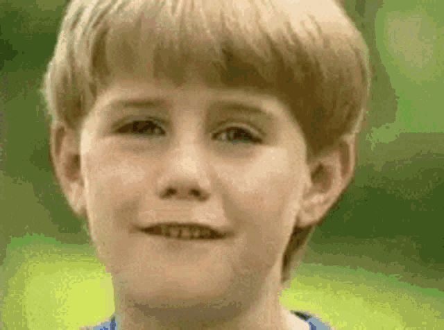 a young boy with blonde hair is smiling for the camera .