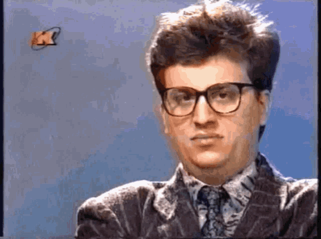 a man wearing glasses and a suit is looking at the camera