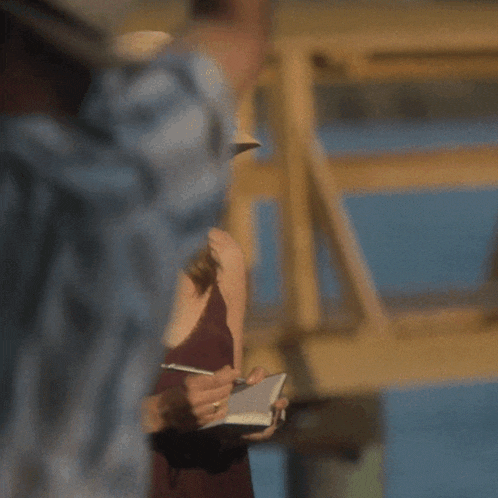 a woman wearing a hat and sunglasses is holding a notebook