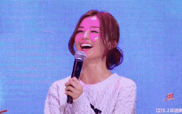 a woman is laughing while holding a microphone in front of her face .