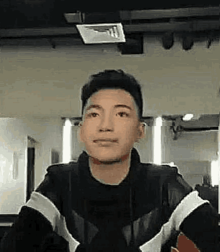a young man in a black jacket is looking at the camera .