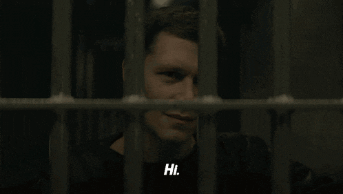 a man in a jail cell behind bars is smiling and says hi