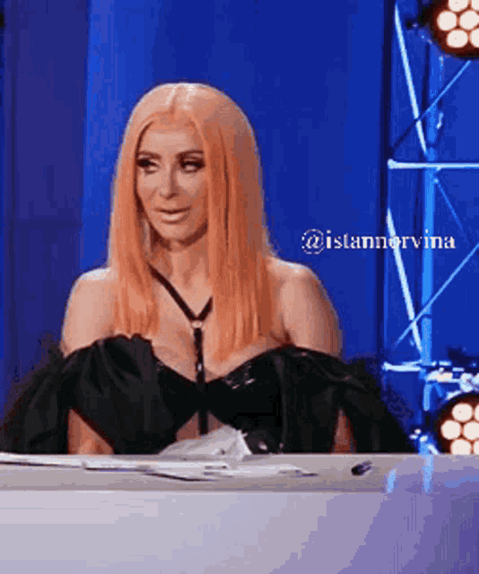 a woman in a black dress is sitting at a table with a blue background and a watermark that says @islanarvina