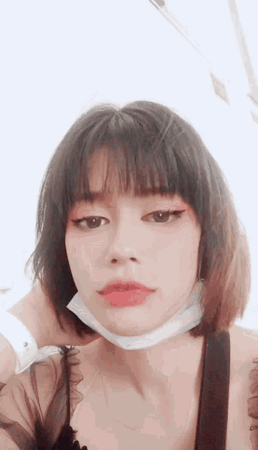 a woman wearing a black top and a white face mask looks at the camera