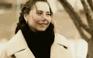 a woman wearing a white coat and a black scarf is smiling