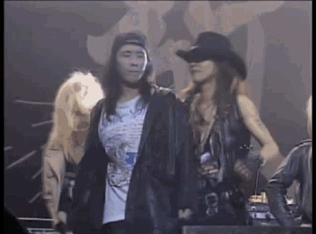 a man with long hair is standing next to a woman in a cowboy hat and holding a microphone .