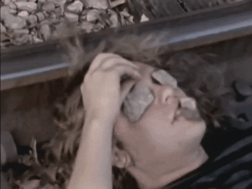 a woman is laying on train tracks with a rock in her eye .