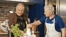 two men in aprons are standing in a kitchen talking to each other