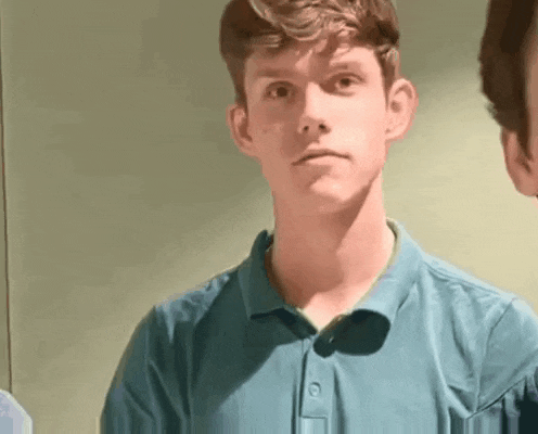 a young man in a blue polo shirt is standing in front of a mirror and looking at the camera .