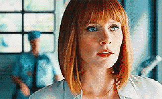a woman with red hair and blue eyes is standing in front of a window with a police officer in the background .