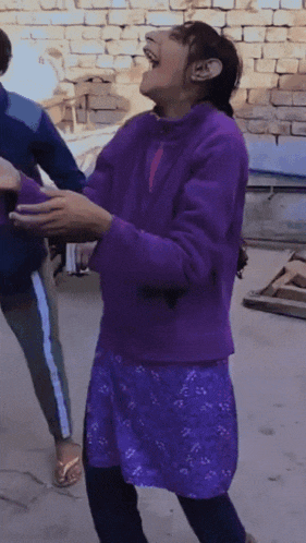a girl in a purple sweater is laughing while standing in front of a brick wall