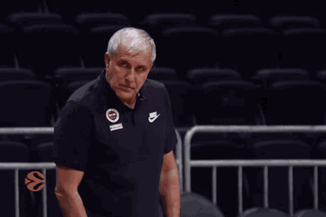 a man wearing a blue nike shirt stands in a basketball arena