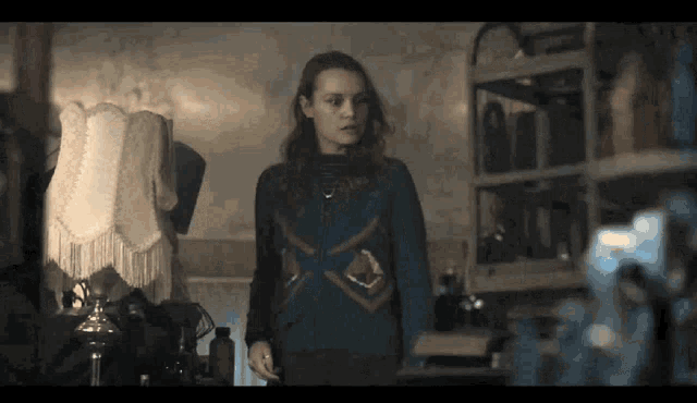 a woman in a blue sweater is standing in a dark room with a lamp .