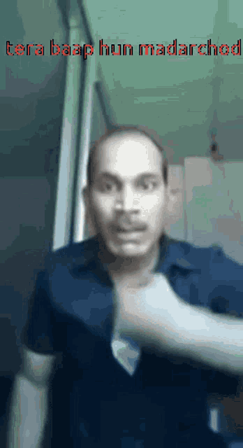 a man in a blue shirt is making a funny face and has the words tera baap hun madarchod written above him