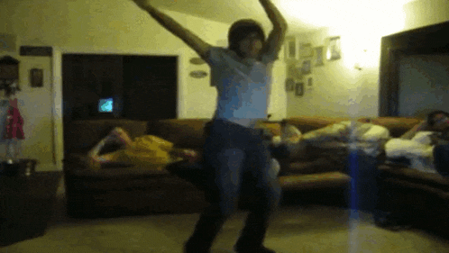 a man in a white shirt is dancing in a living room with a couch in the background