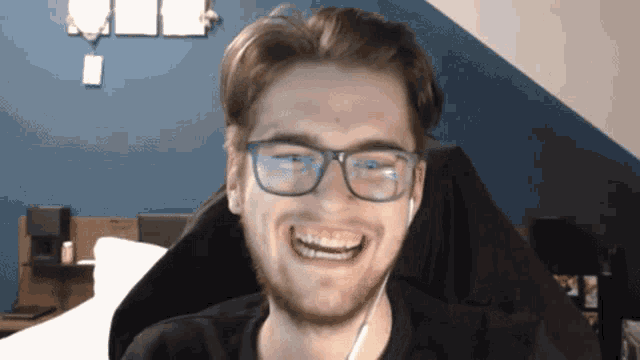 a young man wearing glasses and ear buds smiles for the camera