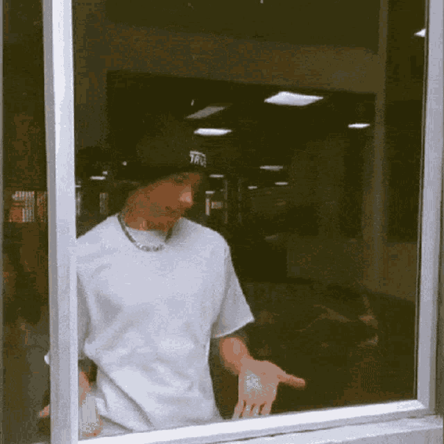 a man in a white shirt and black hat is standing in front of a window with his hands outstretched