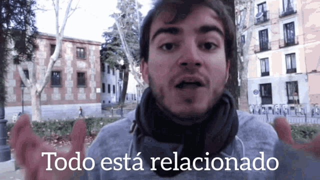 a man with a scarf around his neck stands in front of a sign that says todo esta relacionado