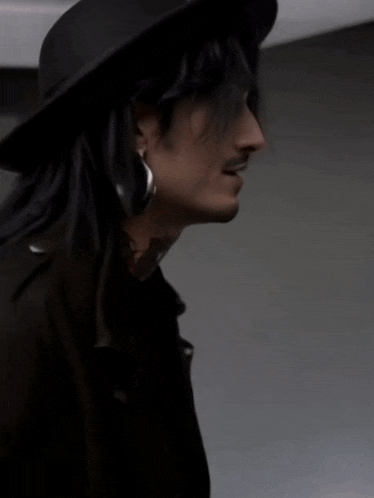 a man with long hair wearing a hat and earrings