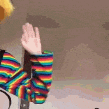 a person in a rainbow striped shirt is waving their hand .