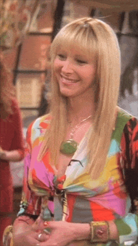 a woman wearing a colorful shirt and a necklace is smiling and looking at the camera .