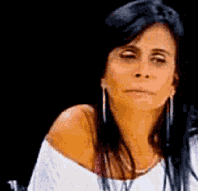a woman wearing a white off the shoulder top and earrings is sitting in a chair .