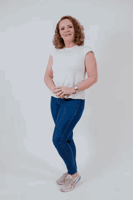 a woman in a white shirt and blue jeans stands with her hands on her hips
