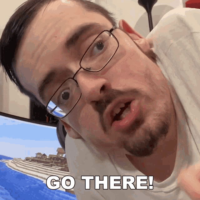a man with glasses and a beard says go there in front of a computer screen