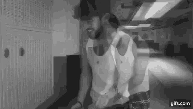 a man in a tank top is standing in a hallway .