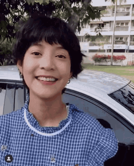 a young woman with short hair is smiling in front of a car .