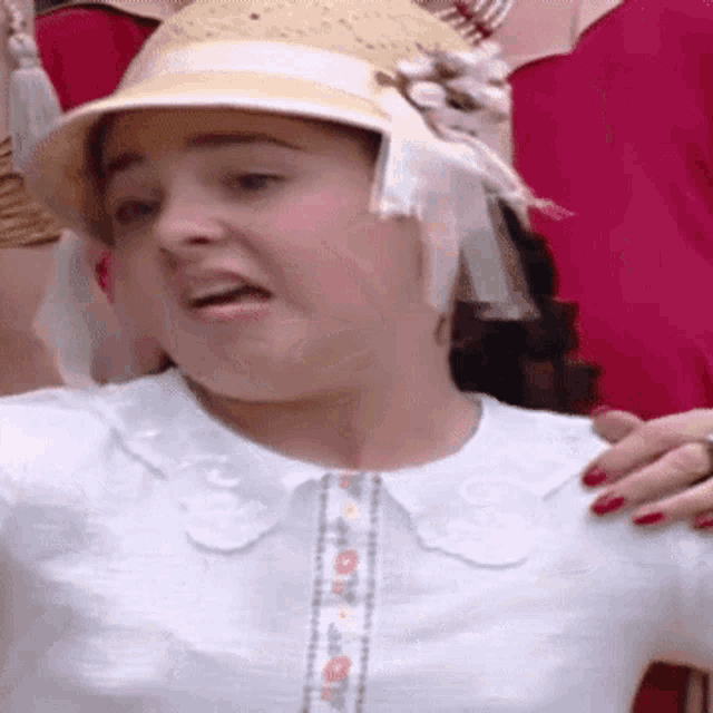 a woman wearing a hat and a white shirt is making a face