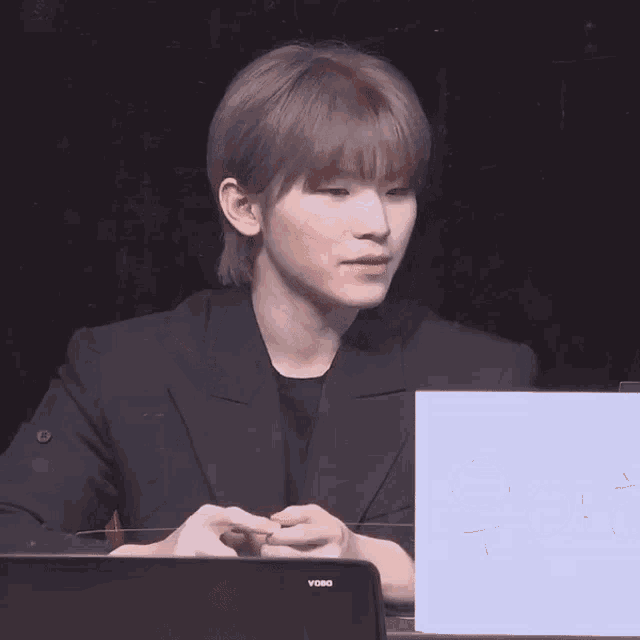 a man in a black suit is sitting at a table with a sign in front of him that says t.