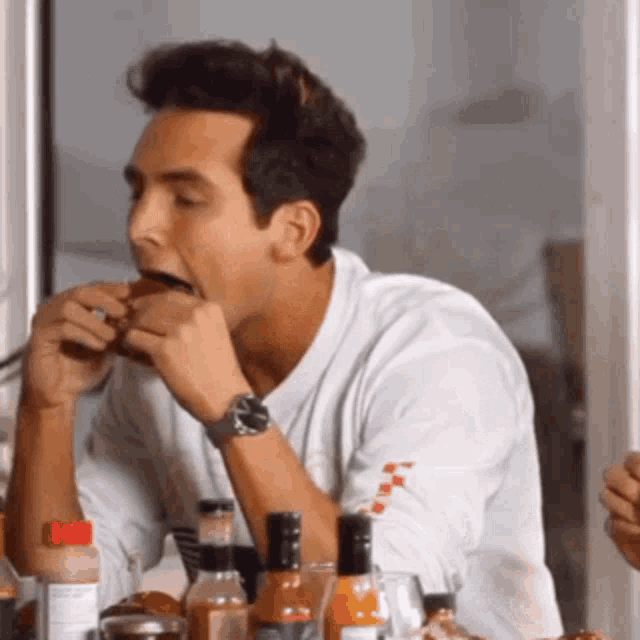 a man wearing a watch is sitting at a table eating a sandwich