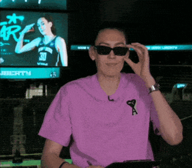 a woman wearing sunglasses and a purple shirt with the letter a on the front