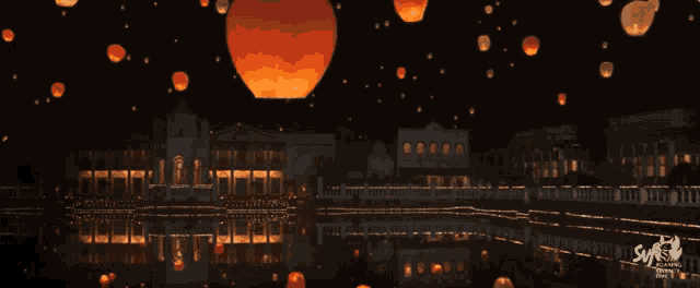 lanterns are floating in the night sky above a city with the sys logo in the lower right corner