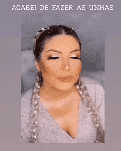 a woman with braids and black nails is wearing a gray sweater and a ring on her finger .