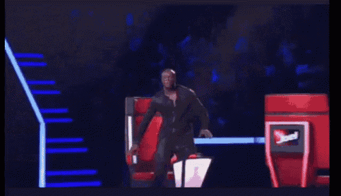 a man in a black suit is standing in front of a red chair with a sign that says ' the voice '