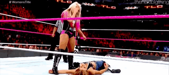 a woman is laying on the ground in a wrestling ring while a referee looks on .
