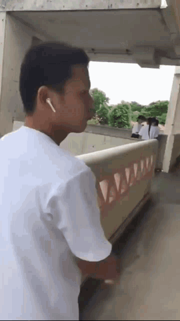 a man wearing ear buds is standing next to a railing in a hallway .