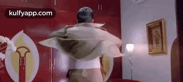a man is standing in a room with a blanket on his back and a picture on the wall .