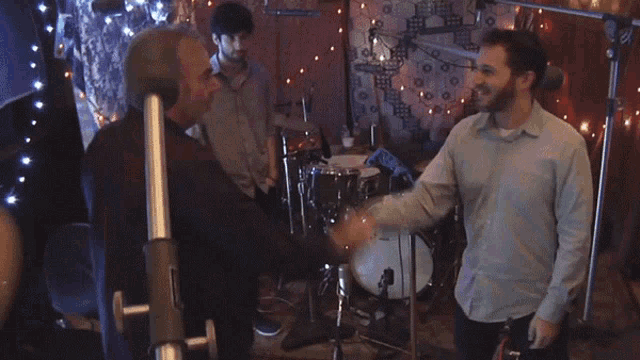 two men shaking hands in a dark room with a drum set in the background