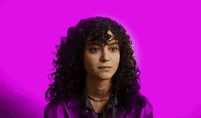 a woman with curly hair is wearing a purple jacket and a necklace .